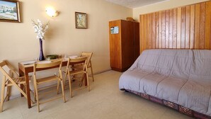 A room with a bed, a wooden wardrobe, a dining table with chairs, and two wall-mounted light fixtures. - Comfortable studio near slopes, 4 people, Wifi, parking (Le Dévoluy)