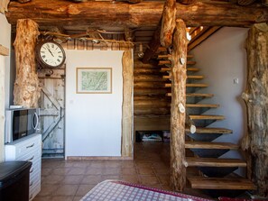 A rustic interior with a wooden staircase, a wall-mounted clock, and a framed map.