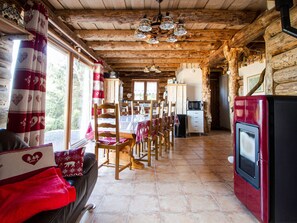 A rustic wooden cabin interior with a dining area, kitchen, and seating by the window.