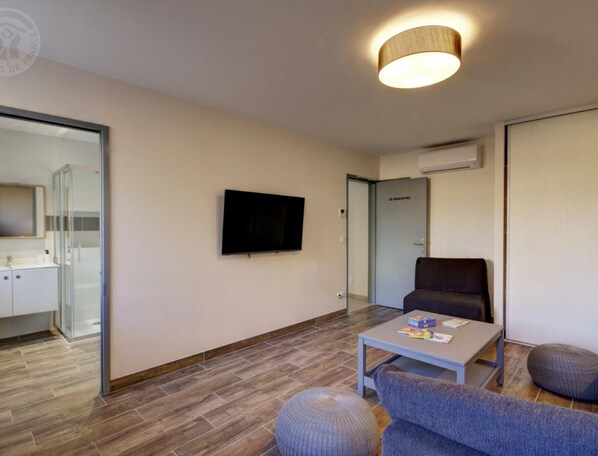 A modern hotel room with a flat-screen TV, a sofa, a small table, and a glass shower enclosure.