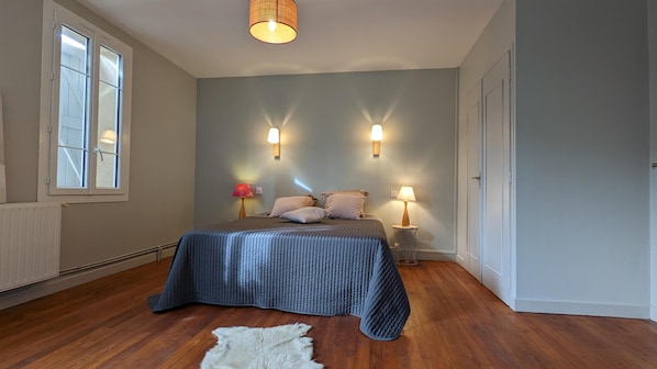A bedroom with a bed, two bedside lamps, a window, and a radiator.