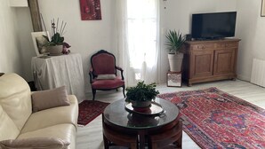 Una sala de estar con un sofá, un sillón rojo, una mesa de centro de vidrio, un televisor y un tapete estampado.