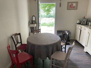 Un comedor con una mesa redonda, sillas rojas y blancas, una zona de cocina con armarios y electrodomésticos, y vistas a zonas verdes.