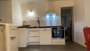 Cocina compacta con muebles blancos, horno empotrado, lavavajillas y refrigerador.