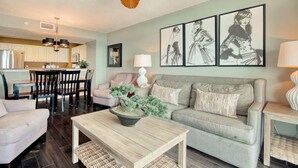 A living room with a sofa, coffee table, and a ceiling fan. There is a dining area with chairs and a table. - Heaven on Earth Summa (Myrtle Beach)
