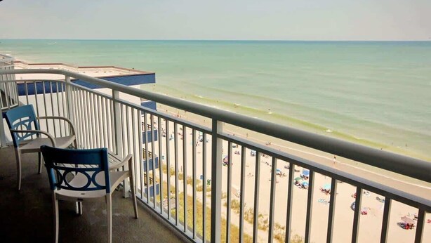 A balcony with a view of the beach, a pool, and outdoor seating. - Heaven on Earth Summa (Myrtle Beach)