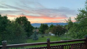 A wooden deck with a view of a grassy yard and mountains in the distance. - Spacious home in the South Hills of Missoula with a great view. (Missoula)