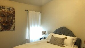 A neatly made bed with white bedding and a grey headboard, a bedside lamp, and a painting on the wall. - Cozy condo located in central Missoula on the Milwaukee Path bike trail. (Missoula)