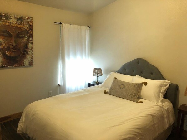 A neatly made bed with white bedding and a grey headboard, a bedside lamp, and a painting on the wall. - Cozy condo located in central Missoula on the Milwaukee Path bike trail. (Missoula)