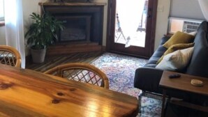 A living room with a wooden dining table, a sofa with cushions, a television on a stand, a ceiling fan, and a large window with curtains. - Cozy condo located in central Missoula on the Milwaukee Path bike trail. (Missoula)