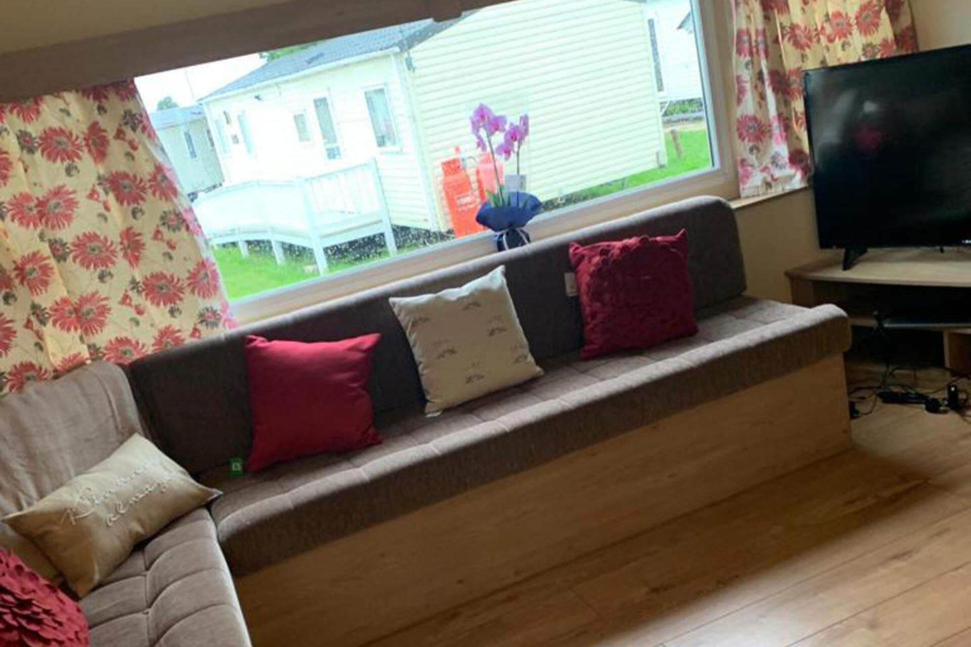 A living room with a sofa, cushions, a television, and a window with a view of a house.