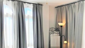 Una camera da letto con un letto, tende grigie, una lampada da comodino e un termosifone.