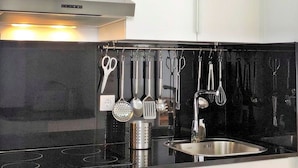 Una cucina moderna con un piano di lavoro nero, elettrodomestici in acciaio inossidabile e diversi utensili esposti a parete.