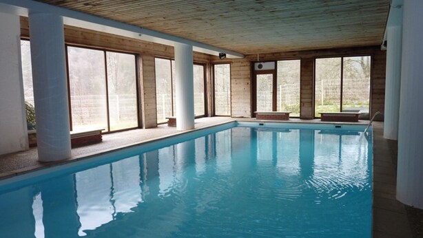 Ein Innenpool mit klarem, blauem Wasser, umgeben von großen Fenstern und Holzbalken.