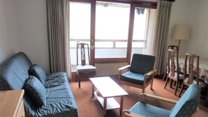 Ein Zimmer mit einer Couch, zwei Sesseln, einem kleinen Tisch, einer Lampe und einem Fenster mit Vorhängen.