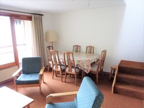 Een kamer met een eettafel, stoelen, een bank en een lamp.