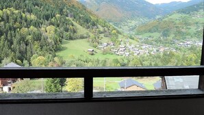 Ein Blick auf ein Tal mit einer kleinen Stadt, eingebettet zwischen Hügeln, sichtbar durch einen Fensterrahmen.