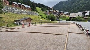 Ein gepflasterter Bereich mit Holzlattenzaun, Steinmauer und Gebäuden im Hintergrund.