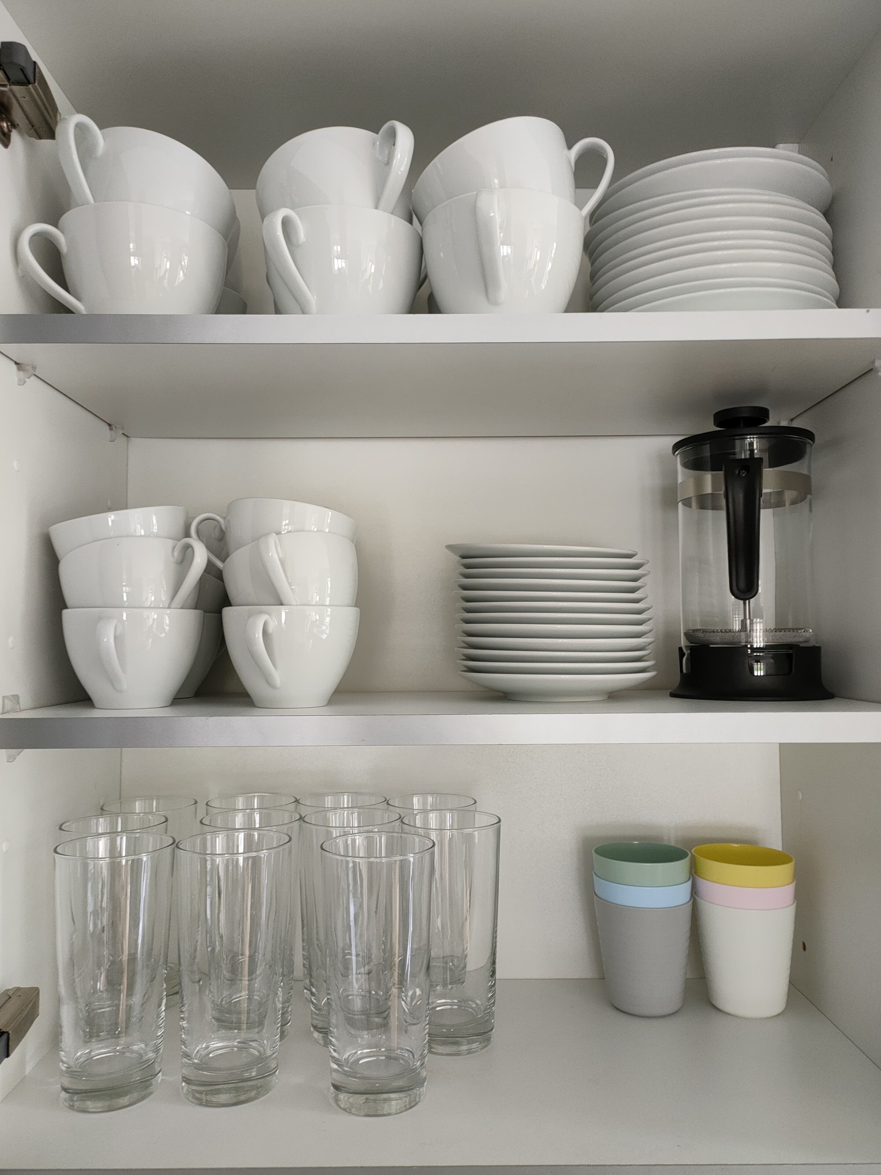 A kitchen shelf with white ceramic cups, plates, and a coffee grinder.