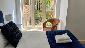 A bedroom with a bed, a chair, and a window with a view of greenery and a stone wall.