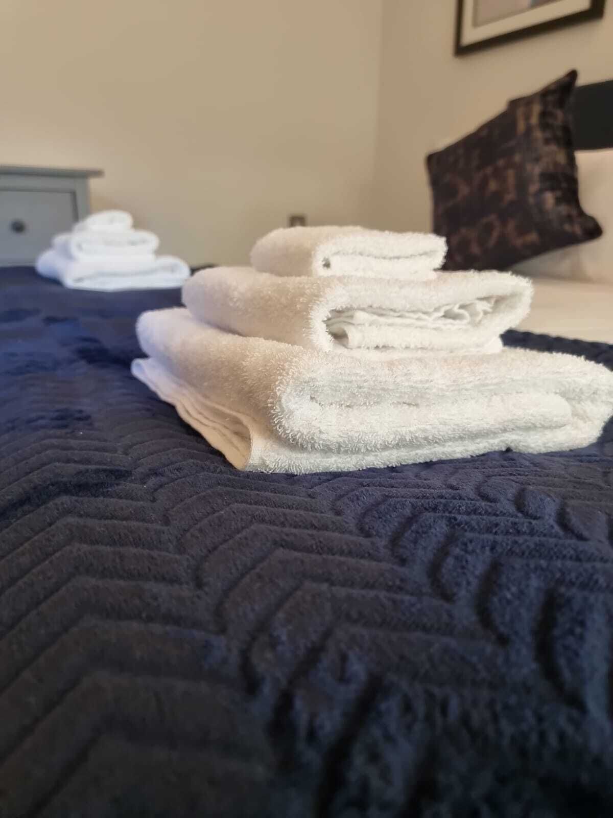A bed with a dark blue quilt and neatly folded white towels.