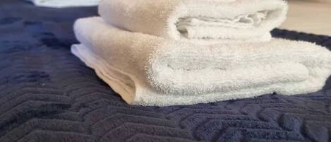 A bed with a dark blue quilt and neatly folded white towels.