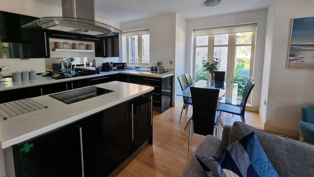A modern kitchen with a central island, black cabinetry, and a large window overlooking a garden.