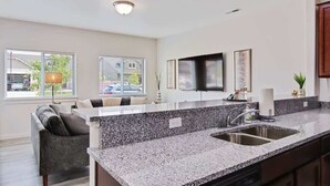 A modern kitchen with granite countertops, a built-in sink, and a dining area with a sofa and chairs. - Charming Centrally Located Treasure Valley Custom (Nampa)
