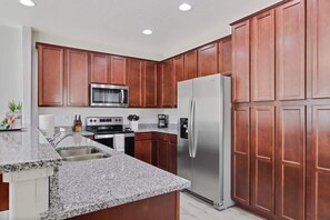 Una cocina con armarios de madera, un refrigerador de acero inoxidable, un microondas y una encimera de granito.