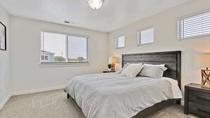 A bedroom with a large bed, two bedside tables, a ceiling light, and three windows with blinds. - Charming Centrally Located Treasure Valley Custom (Nampa)