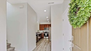 A hallway leading to a kitchen with wooden cabinets, a stainless steel refrigerator, and a microwave. - Charming Centrally Located Treasure Valley Custom (Nampa)