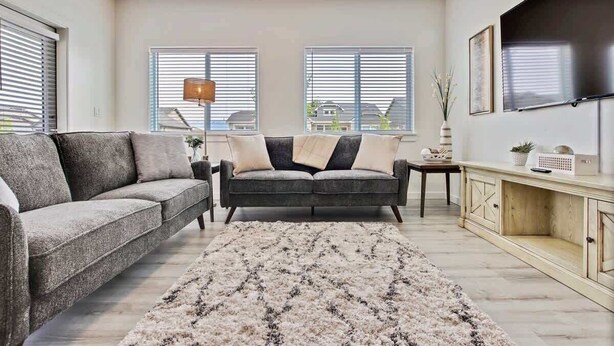A living room with two sofas, a coffee table, a TV, and a large window with blinds. - Charming Centrally Located Treasure Valley Custom (Nampa)