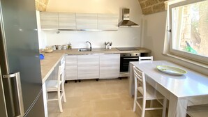A kitchen with a brick ceiling, white cabinets, a stainless steel refrigerator, and a dining area with a table and chairs. - Villa dei Desideri (Salve)