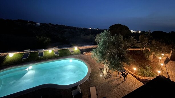 A swimming pool with lounge chairs and a tree, surrounded by stone walls and lights. - Villa dei Desideri (Salve)