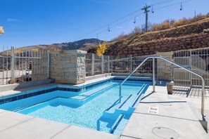 Une piscine avec un mur en pierre, une rambarde en métal et un ciel bleu clair en arrière-plan.