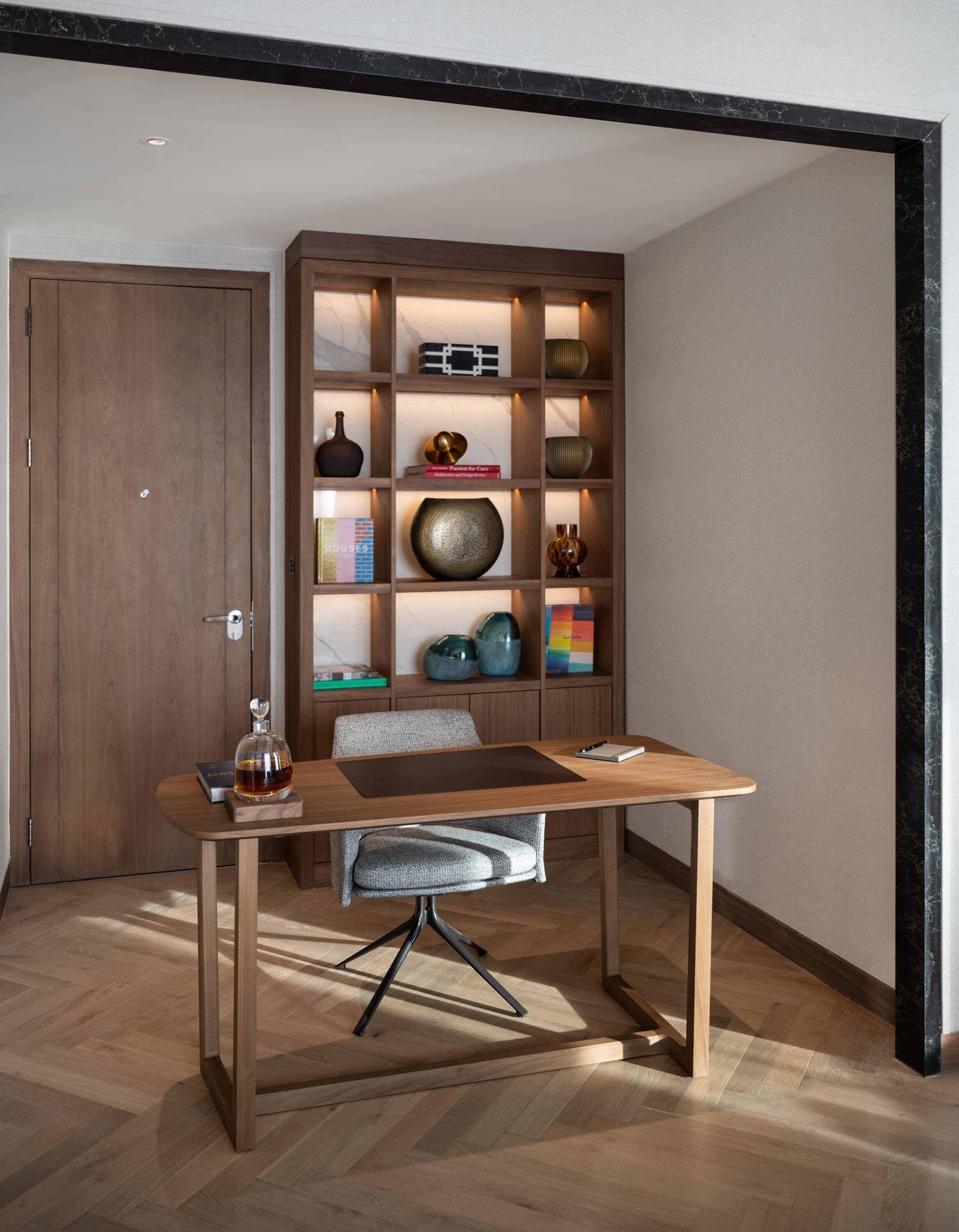 Un comedor moderno con una mesa y sillas de madera, una estantería empotrada con objetos decorativos y una puerta de madera al fondo.