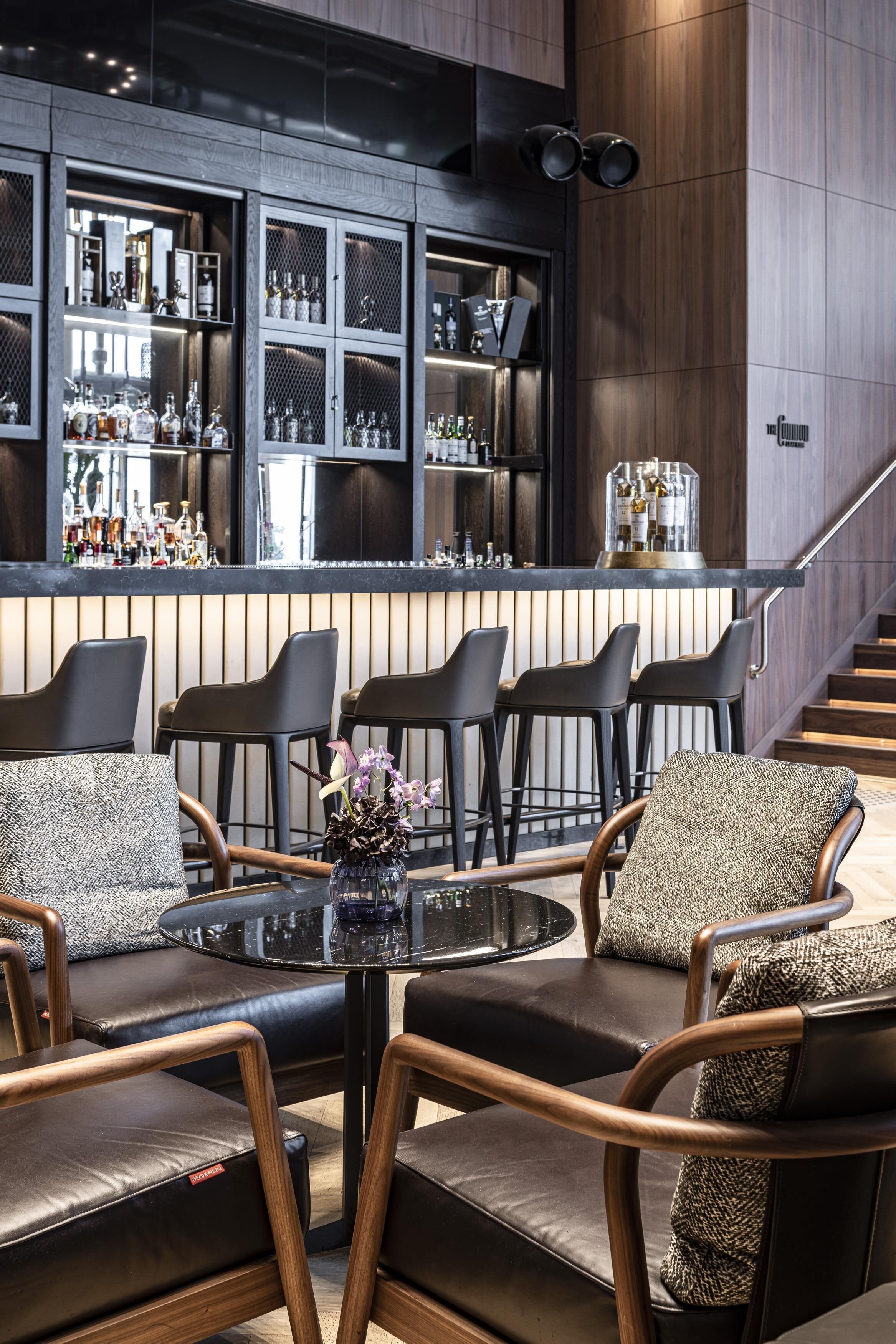 A modern bar area with a round table and leather chairs, a staircase, and a bar stocked with bottles.