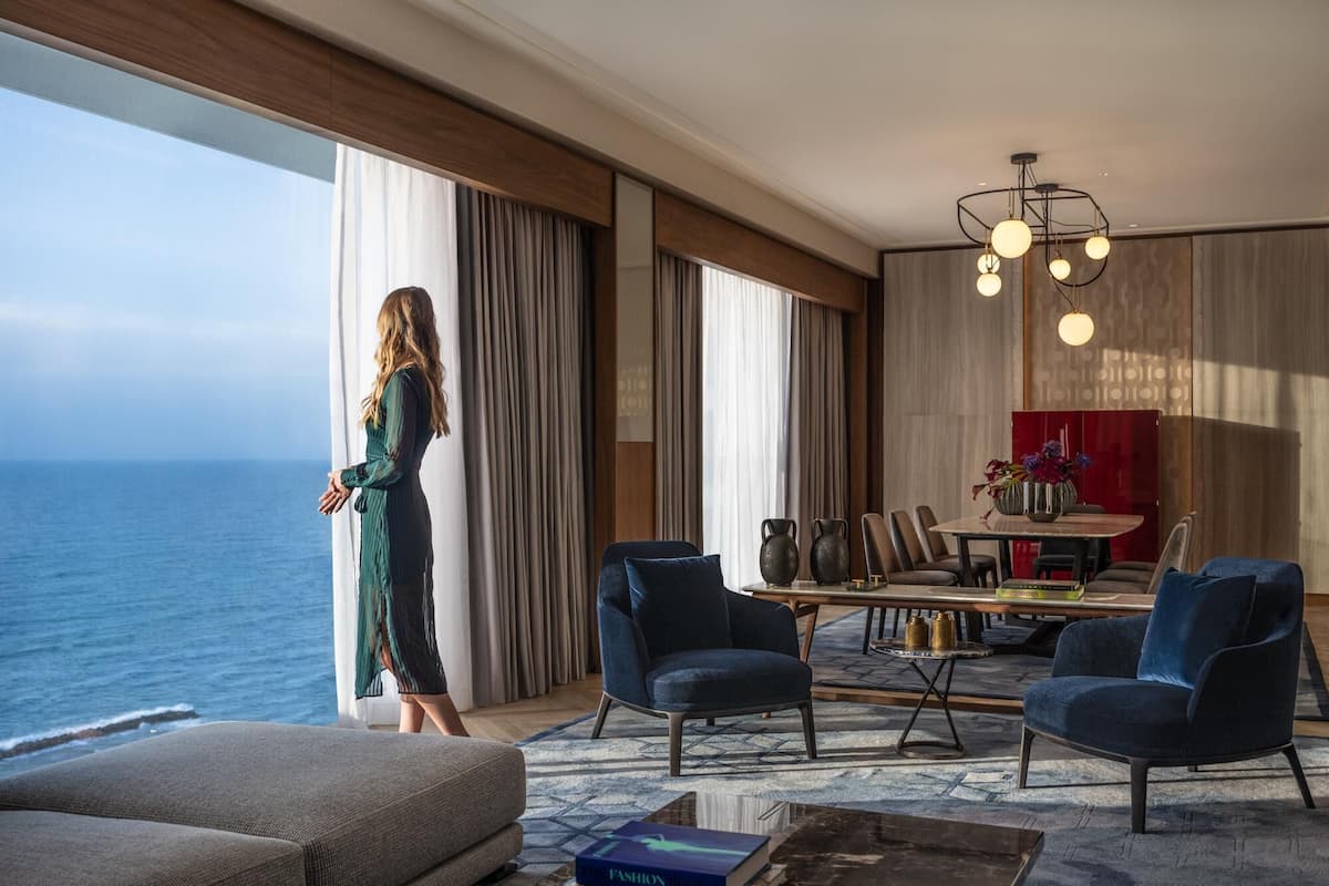 Une pièce spacieuse dotée d’une grande fenêtre donnant sur la mer, un coin repas avec des meubles modernes et un élégant lustre.