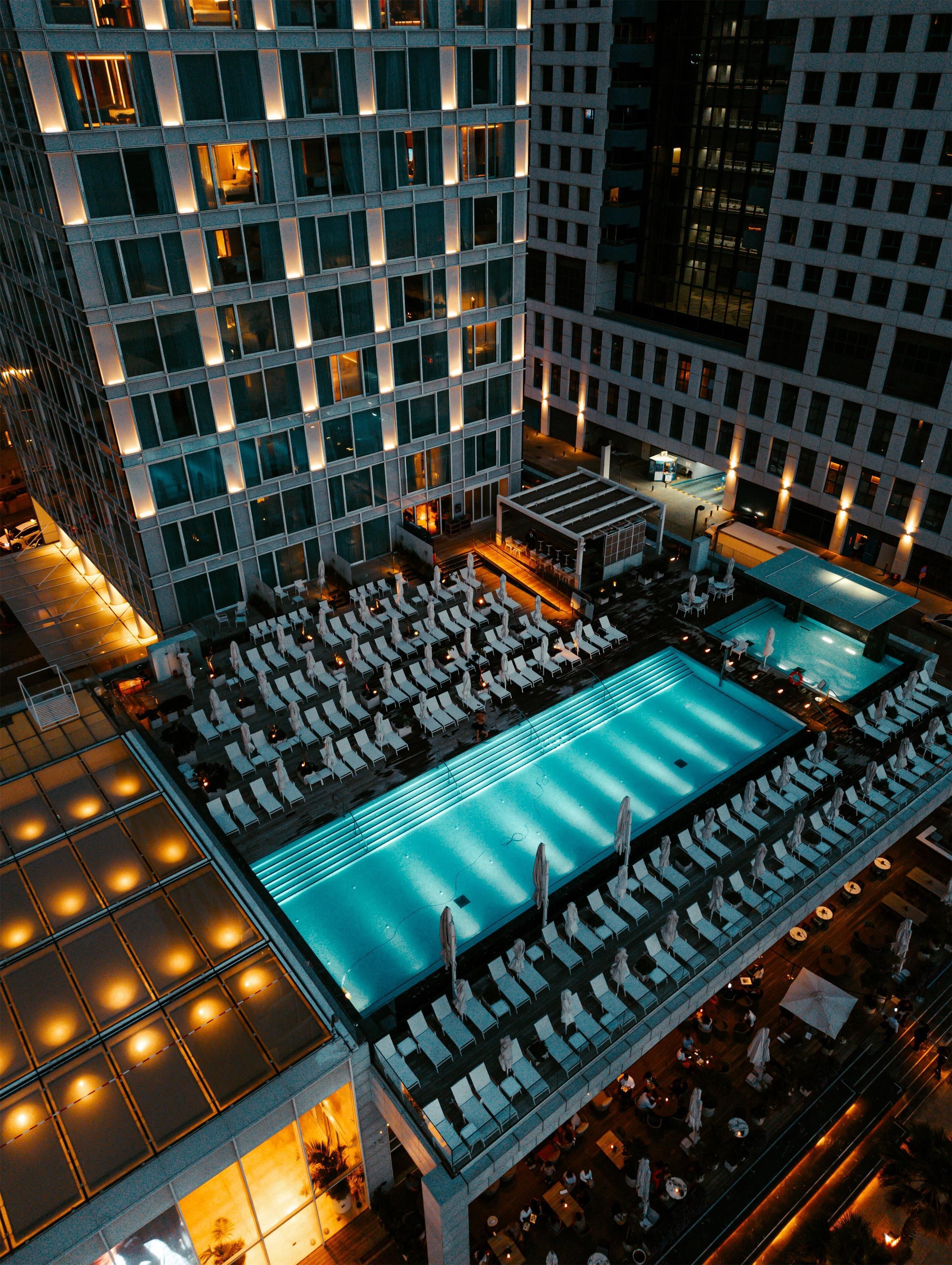 Un hotel moderno de gran altura con piscina en la azotea, varias opciones de restauración y una fachada bien iluminada.