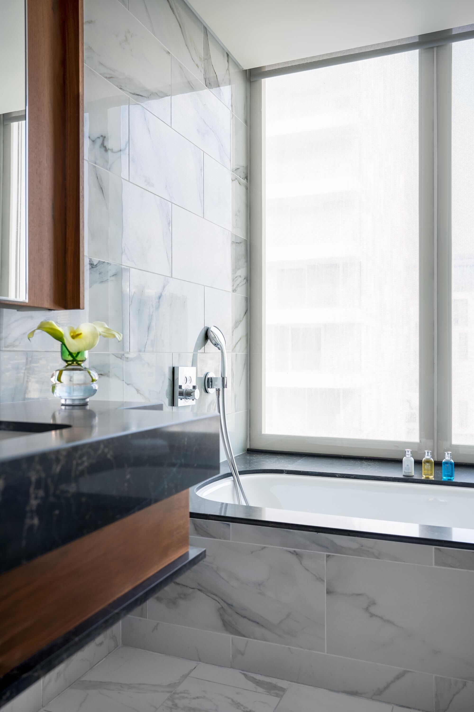 A modern bathroom with a marble sink, a large window, and a vase with flowers.