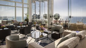 Un espacio lounge moderno con ventanas amplias, asientos cómodos y plantas decorativas.