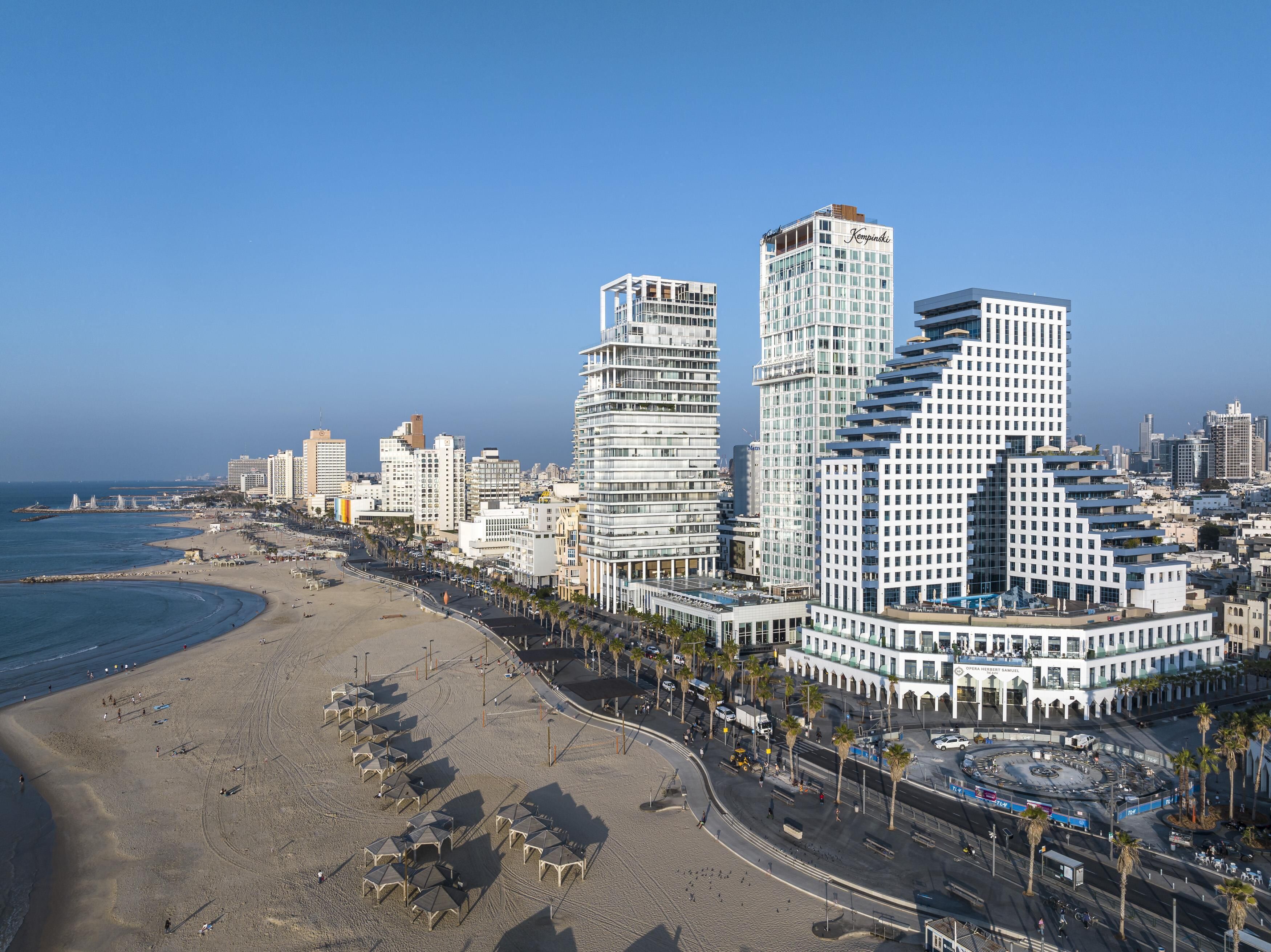 Un paysage urbain côtier avec des immeubles modernes de grande hauteur, une plage et une promenade bordée de palmiers.