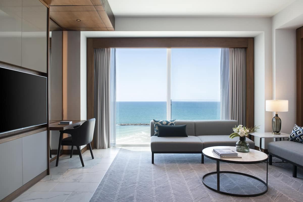 Une chambre d’hôtel moderne dotée d’une grande fenêtre, d’un canapé, d’une table basse, d’un téléviseur et d’un bureau.