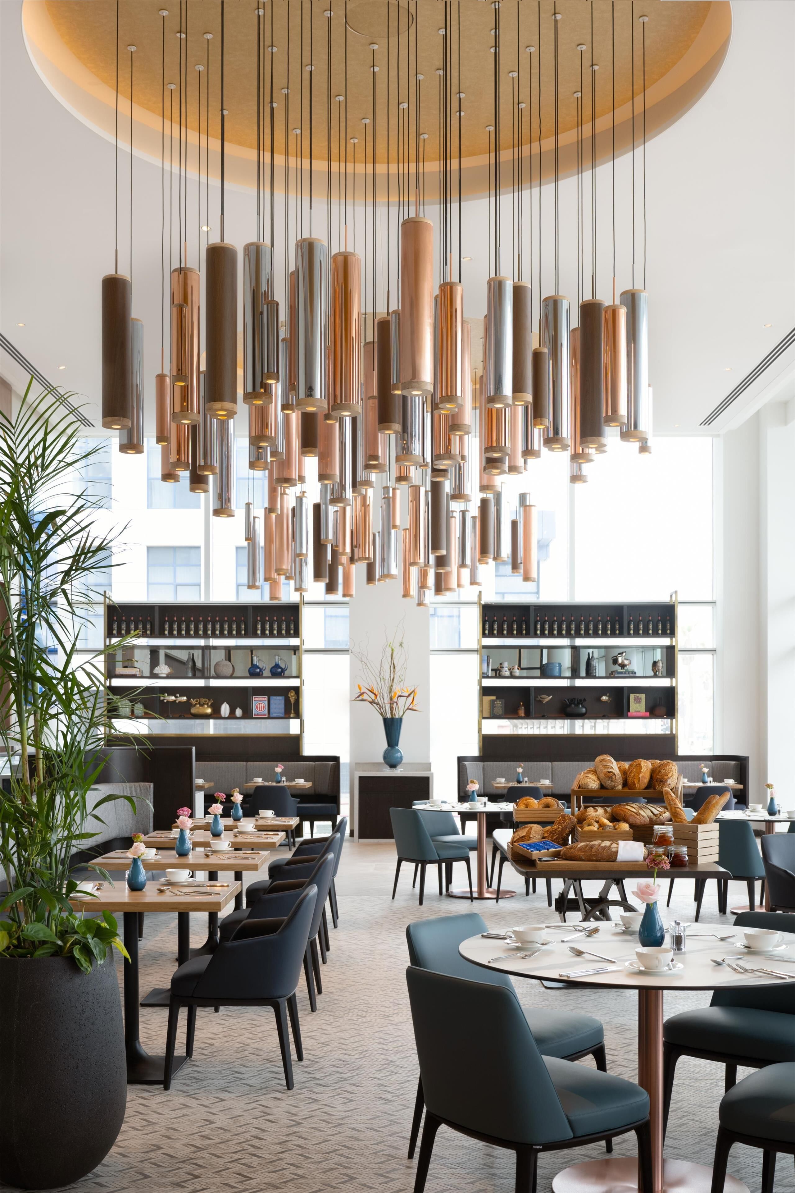 Un comedor moderno con varias mesas y sillas, un área de estar central y diversos elementos decorativos.