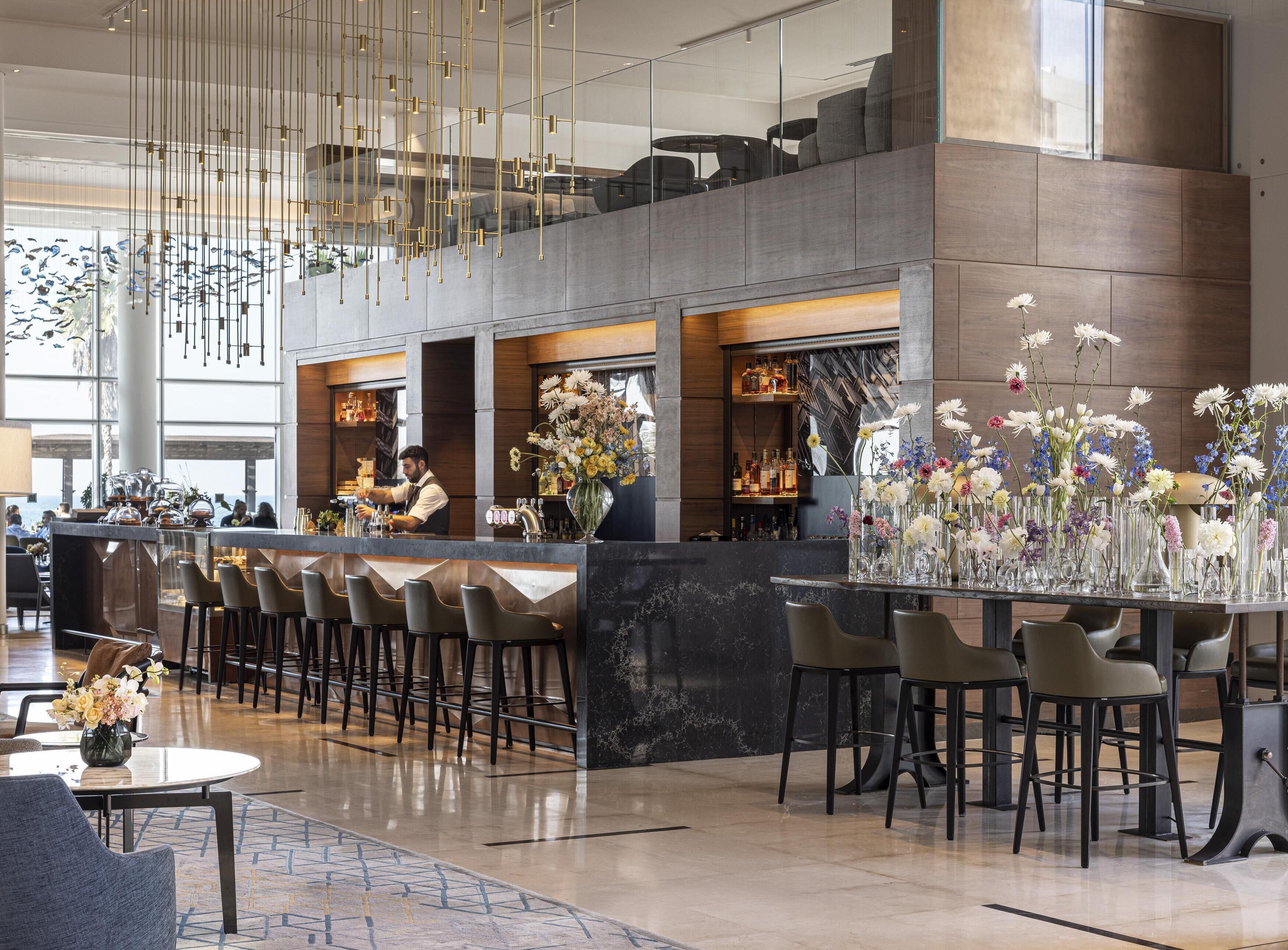 A modern bar area with a bartender, multiple seating arrangements, and a large floral centerpiece.