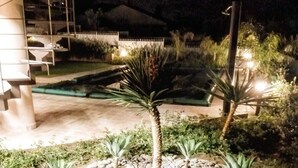 Ein Garten bei Nacht mit einer Palme und Sukkulenten, umgeben von Kieselsteinen, einer Treppe und einem Gebäude im Hintergrund.