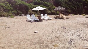 Ein Strand mit weißen Liegestühlen und einem Strohdachschirm.