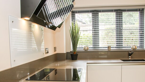 Une cuisine moderne avec une plaque de cuisson à induction noire, une plante en pot et une fenêtre avec des stores.
