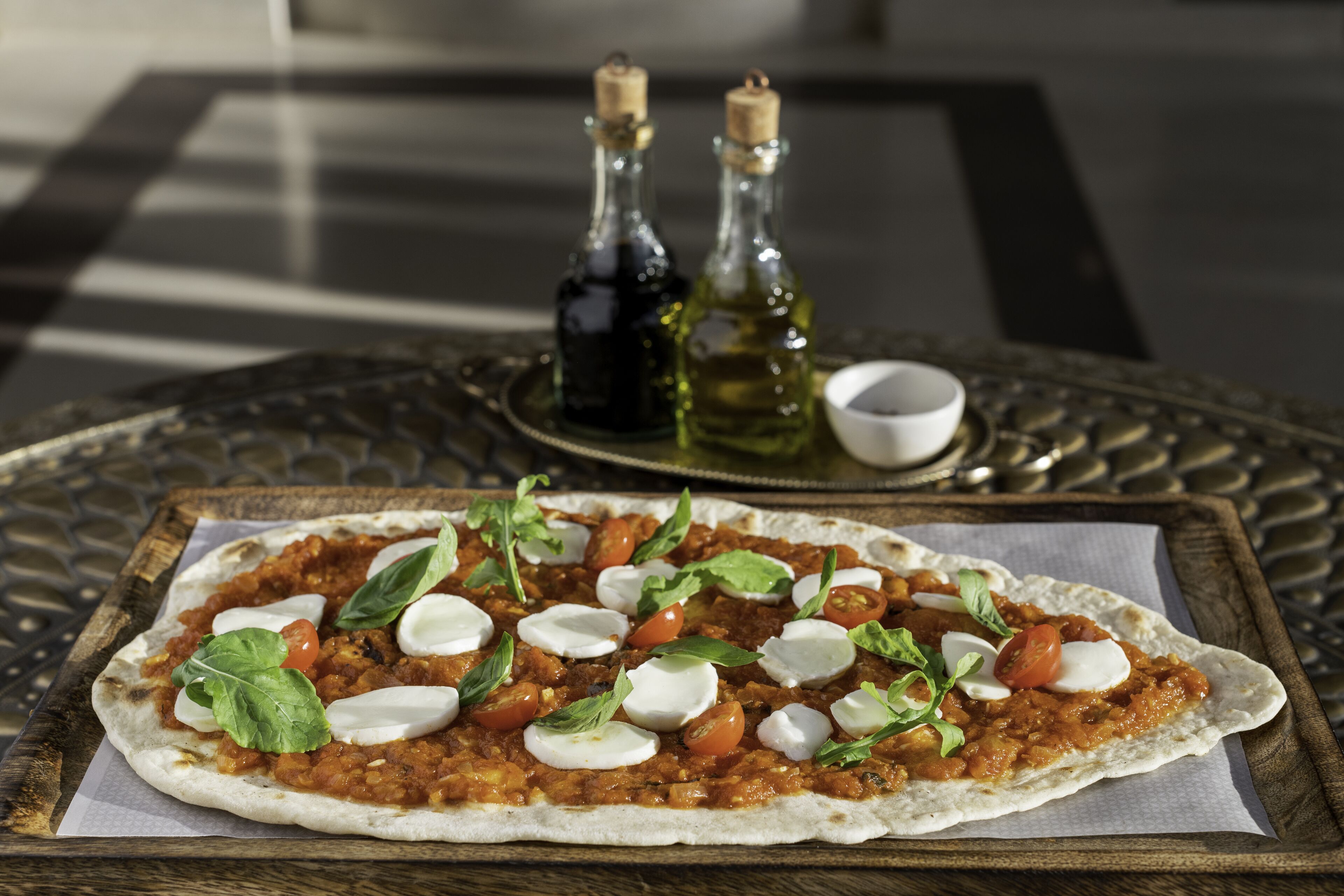 A pizza on a wooden tray with a checkered tablecloth.
