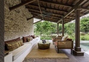 A covered outdoor seating area with a brick wall, wooden ceiling, and a view of a garden and pool. - Aramness Gir National Park (Mendarda)